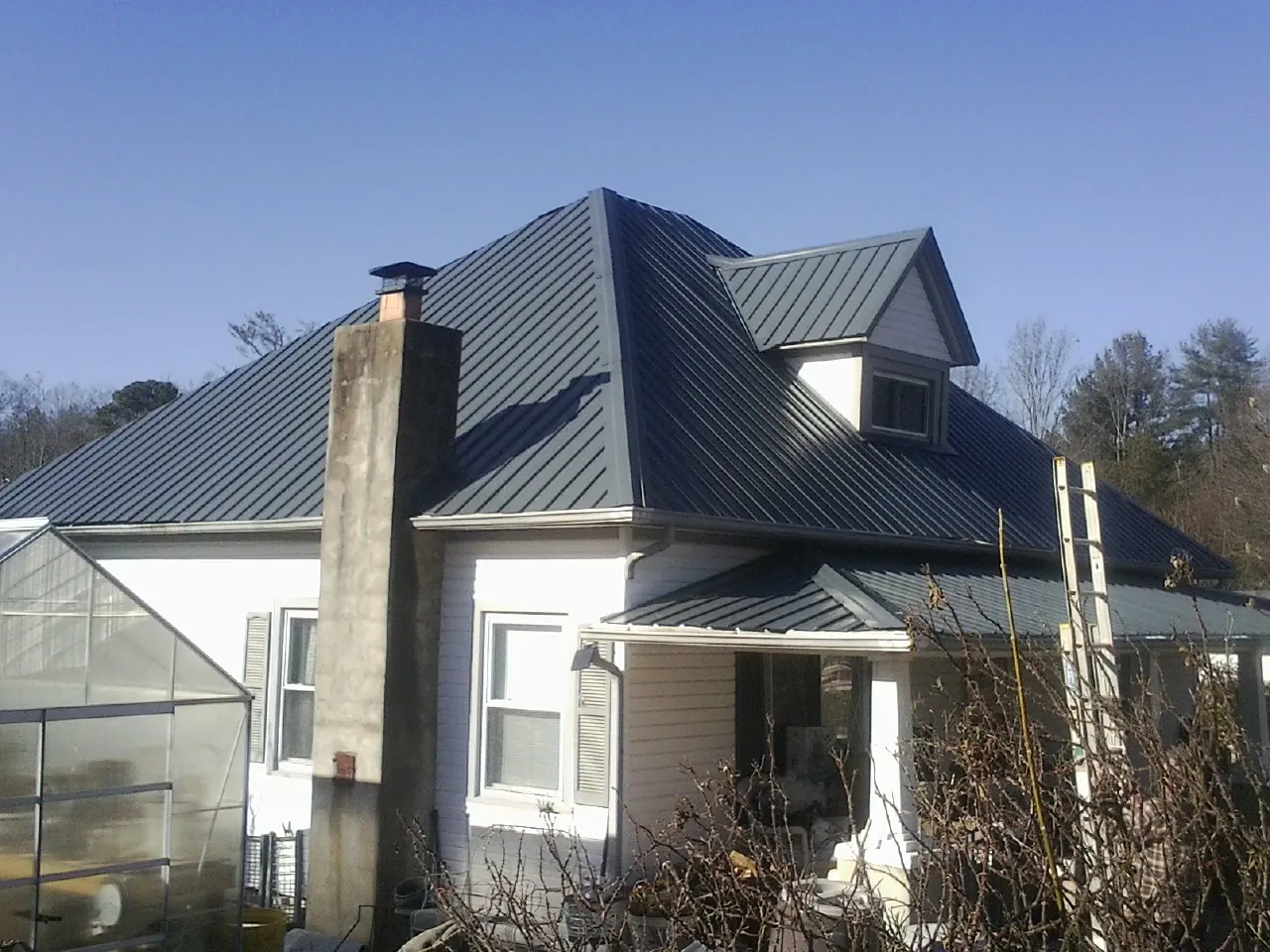 Dark blue standing seam metal roof on a white farmhouse with dormer — Slate & Tile Roof Repair by Roofing Brothers in Gouldsboro