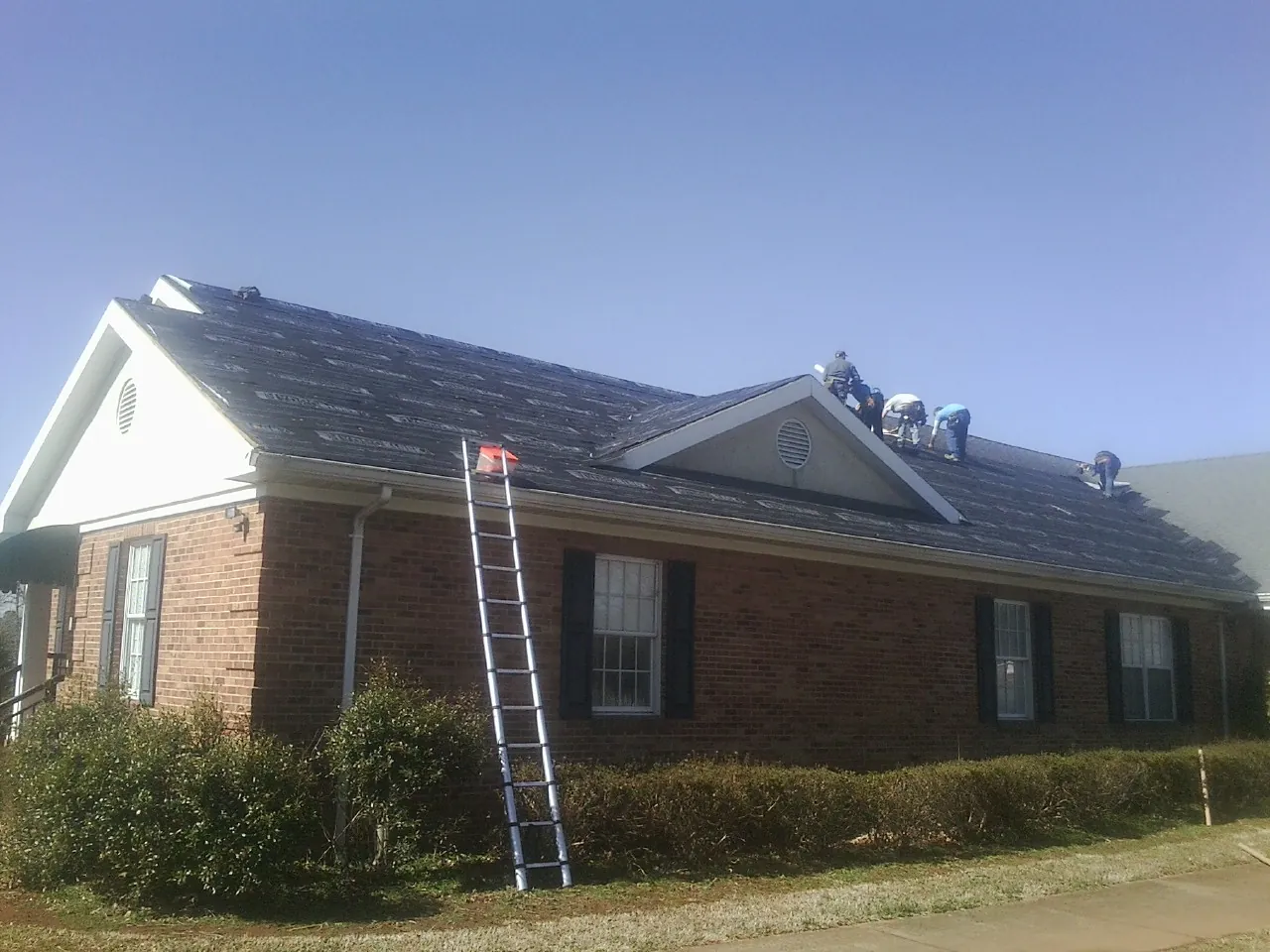 Crew tearing shingles off a brick ranch roof with a ladder set — Metal Roof Repair work by our crew in Gouldsboro