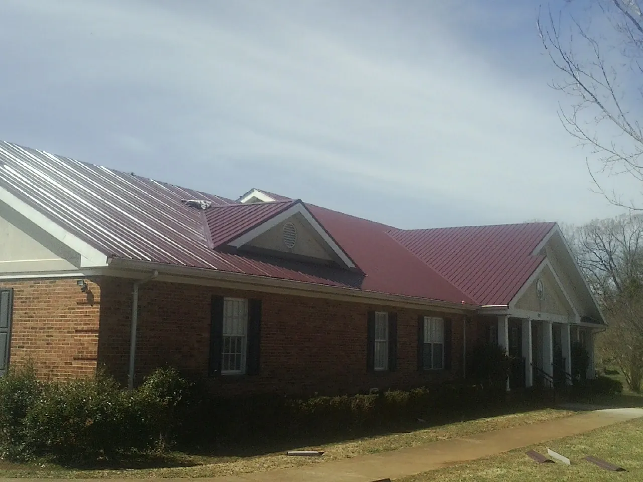 Red metal roof with gabled entries on a long brick building, from a Hail Damage Roof Repair job in Gouldsboro