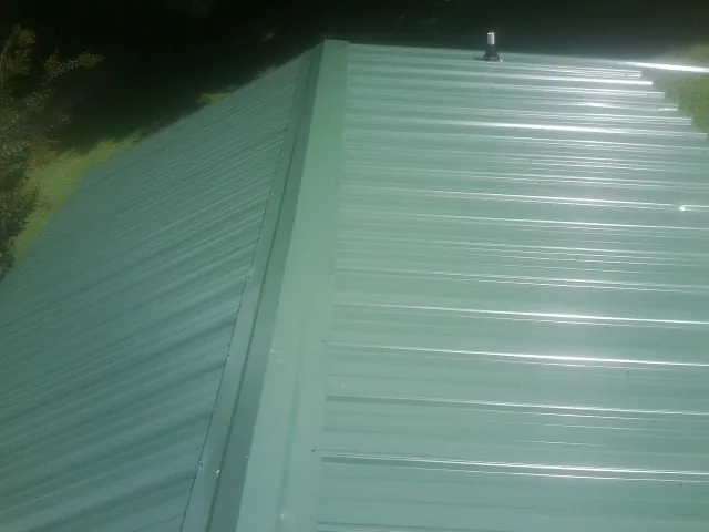 New green metal panels meeting at the ridge of a roof — Flat Roof Repair work by our crew in Gouldsboro