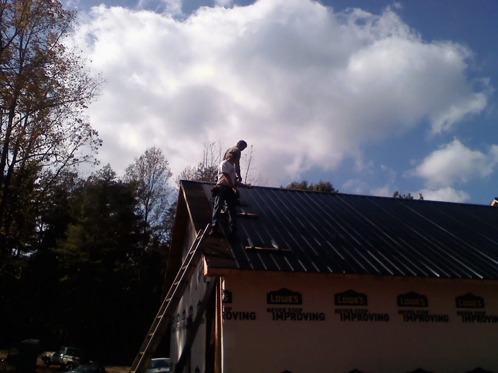 Roofer fastening dark metal panels high against a cloudy sky, from a Roof Inspection job in Gouldsboro