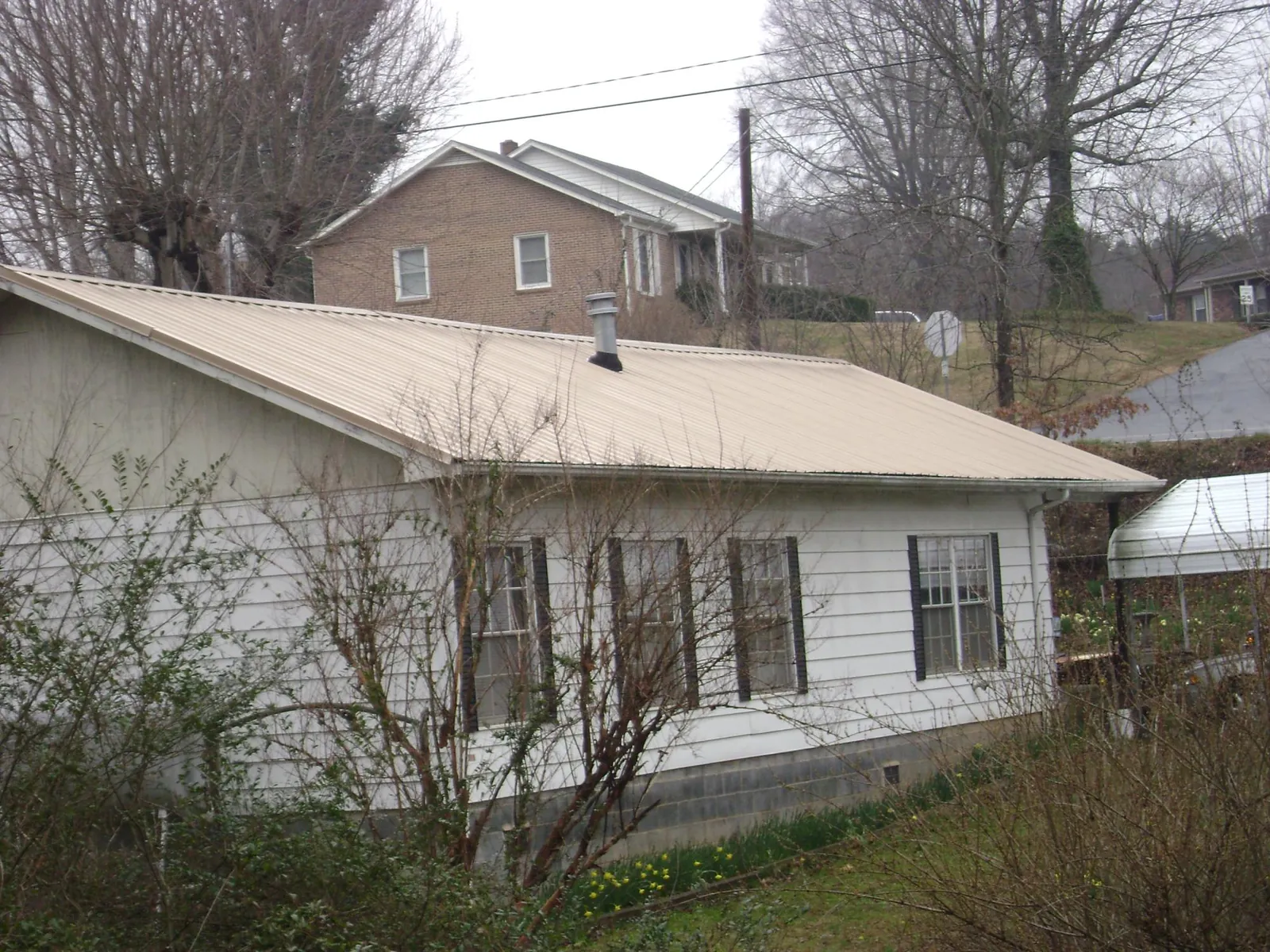 Tan metal roof on a white sided house set into a hillside — Commercial Roofing by Roofing Brothers in Gouldsboro